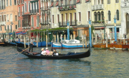 A gondolier rows a long black gondola past waterfront buildings on Venice&rsquo;s Grand Canal.