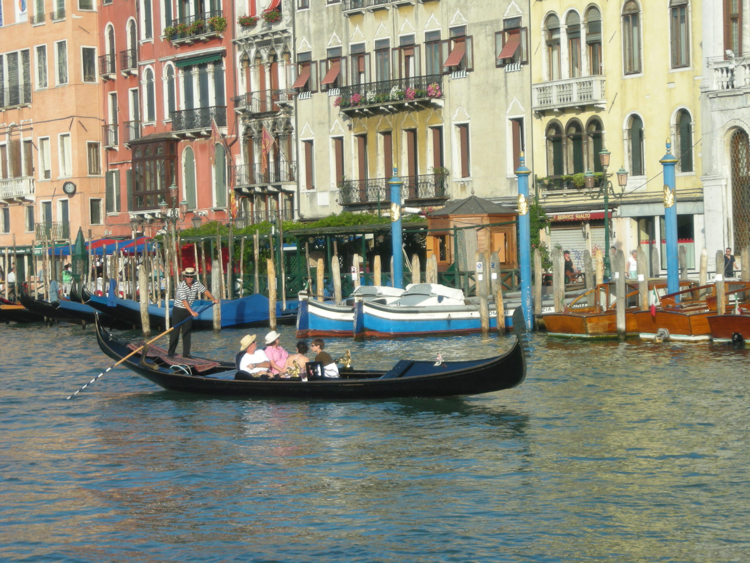 A gondolier rows a long black gondola past waterfront buildings on Venice’s Grand Canal.