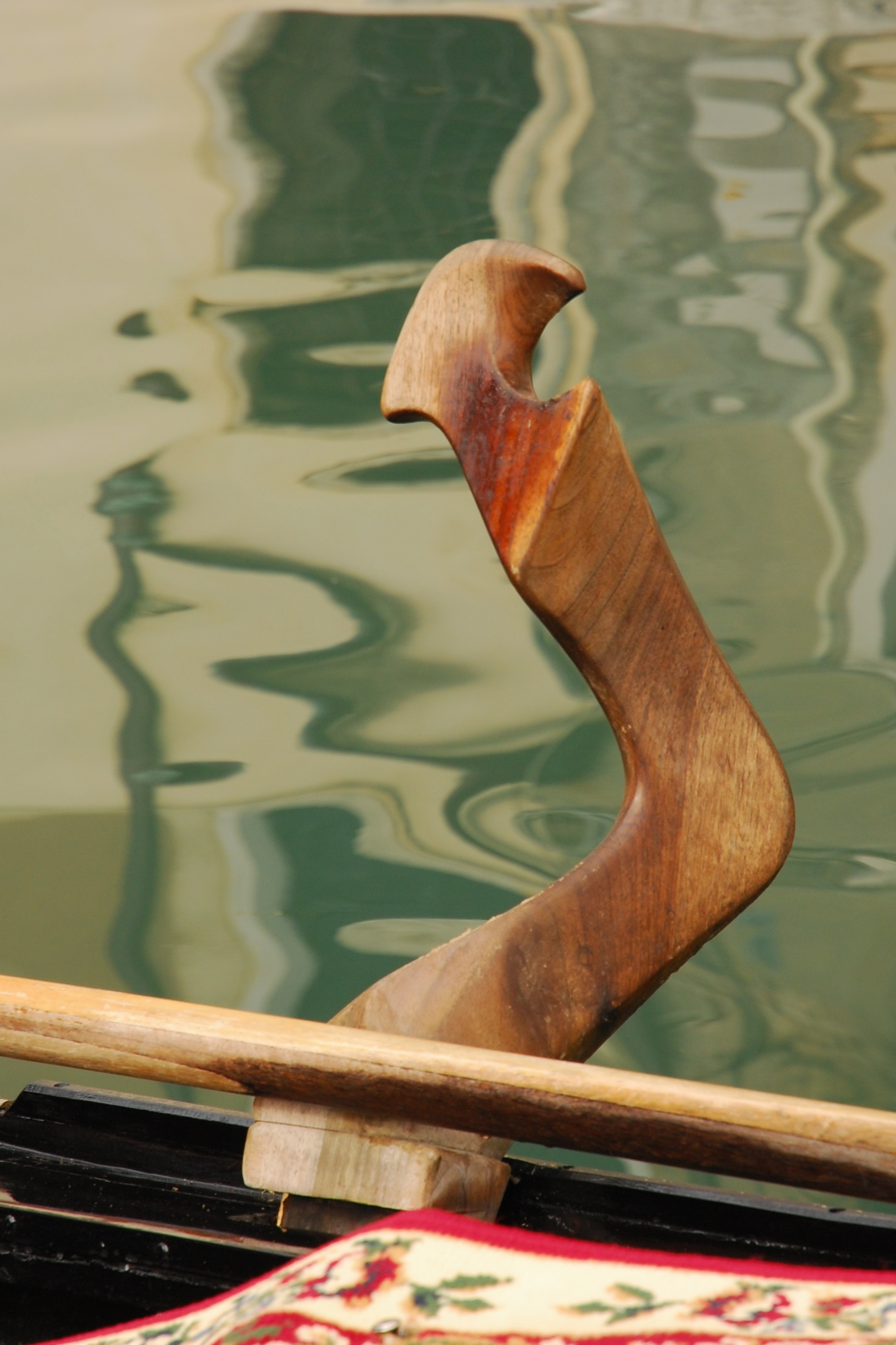 Close-up of the curved wooden fórcola mounted on a Venetian gondola, with an oar across its base.