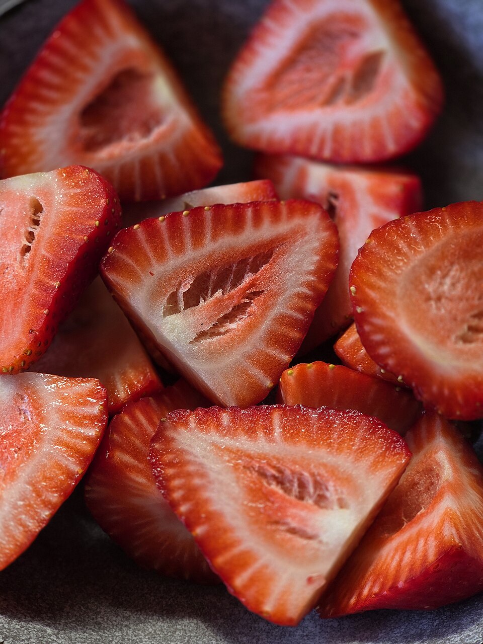 Cut strawberry pieces showing red flesh, pale centers and achenes along their outer edges.